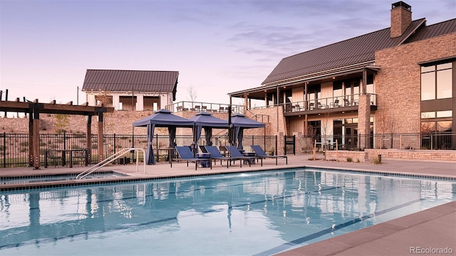 pool at dusk with fence, a community pool, and a gazebo