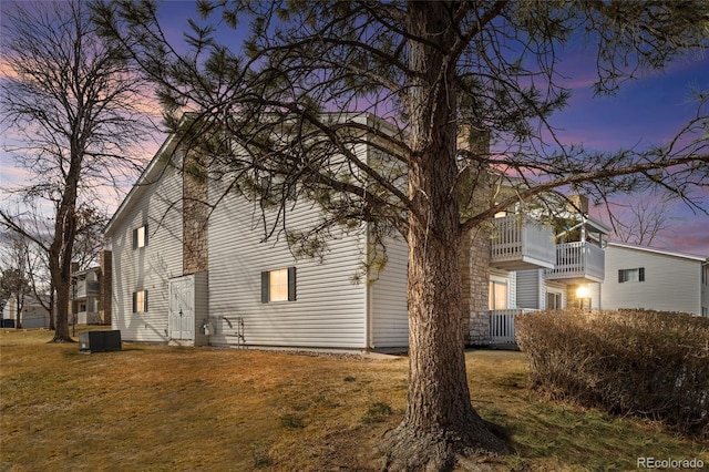 property exterior at dusk with a balcony, a lawn, and central air condition unit