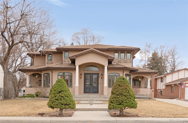 mediterranean / spanish home with a tiled roof, stucco siding, and french doors