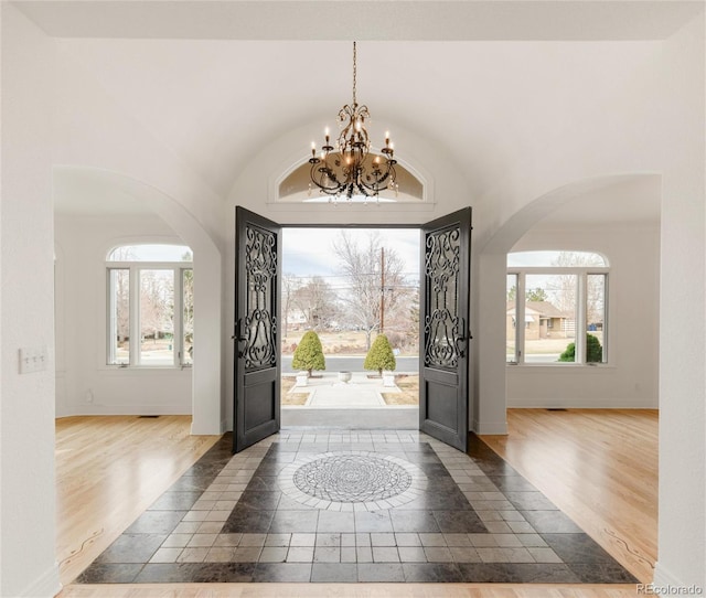 entryway with a notable chandelier, vaulted ceiling, baseboards, and wood finished floors