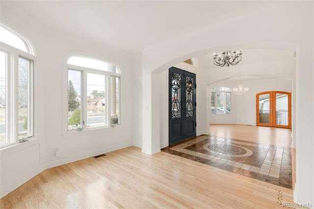 entryway featuring visible vents, wood finished floors, french doors, arched walkways, and a chandelier