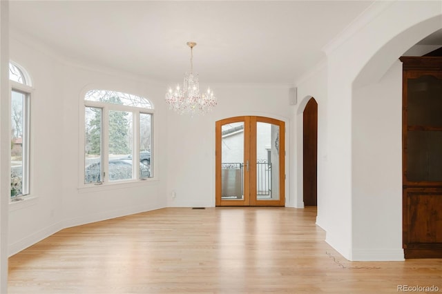 spare room with ornamental molding, french doors, arched walkways, light wood finished floors, and baseboards