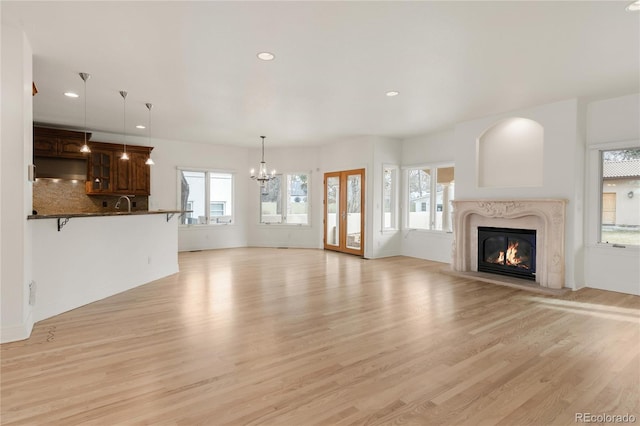 unfurnished living room featuring light wood-style flooring, a notable chandelier, recessed lighting, and a premium fireplace