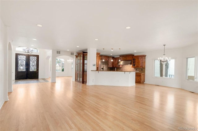 unfurnished living room with light wood-style flooring, recessed lighting, arched walkways, french doors, and a chandelier