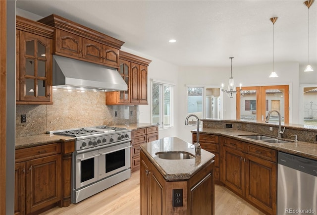 kitchen featuring a sink, dark stone countertops, under cabinet range hood, and stainless steel appliances