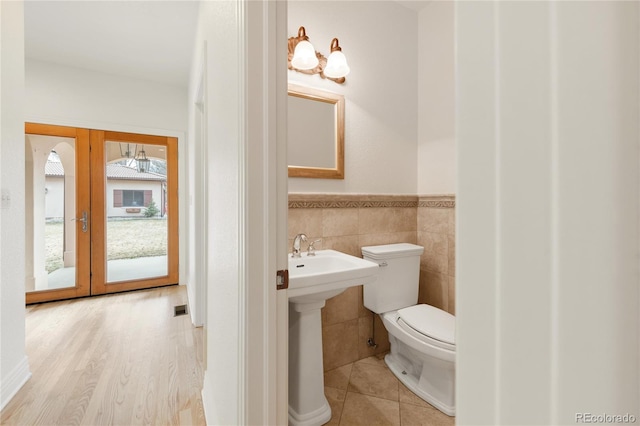 bathroom with a sink, french doors, wainscoting, tile walls, and toilet