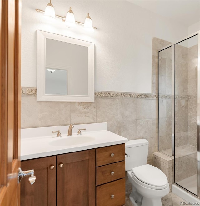 bathroom featuring toilet, a stall shower, vanity, and tile walls