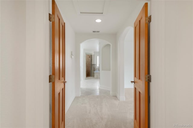 hall featuring visible vents, light carpet, arched walkways, and baseboards