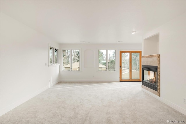 unfurnished living room featuring a tiled fireplace, carpet flooring, and baseboards