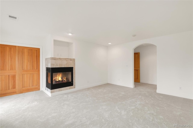 unfurnished living room with visible vents, carpet floors, baseboards, a fireplace, and arched walkways