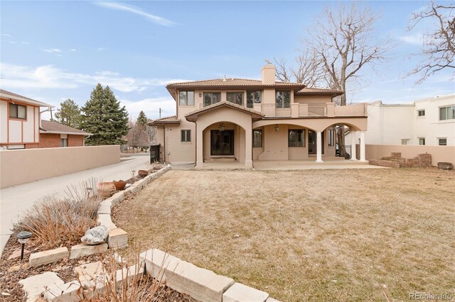 back of property featuring a balcony, fence, a chimney, stucco siding, and a tiled roof