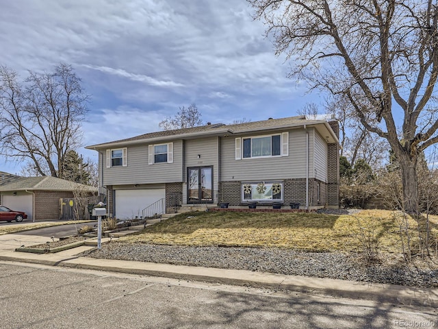 bi-level home featuring a garage, driveway, brick siding, and a chimney