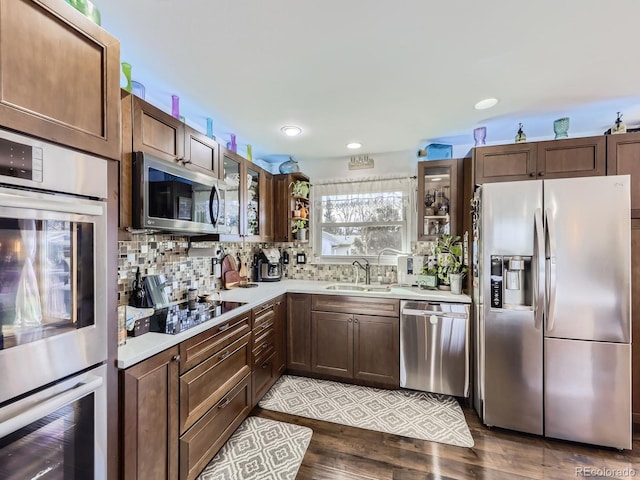 kitchen featuring stainless steel appliances, a sink, light countertops, decorative backsplash, and glass insert cabinets