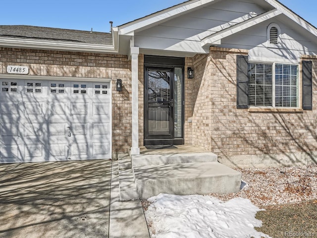 view of exterior entry featuring concrete driveway, brick siding, and an attached garage