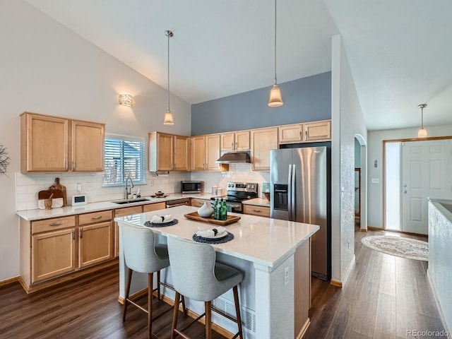 kitchen with arched walkways, under cabinet range hood, a sink, appliances with stainless steel finishes, and light brown cabinetry