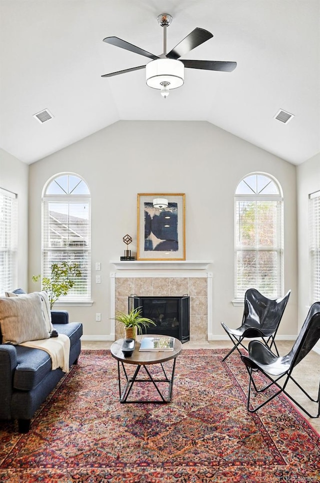 living area featuring a ceiling fan, visible vents, a tiled fireplace, and lofted ceiling
