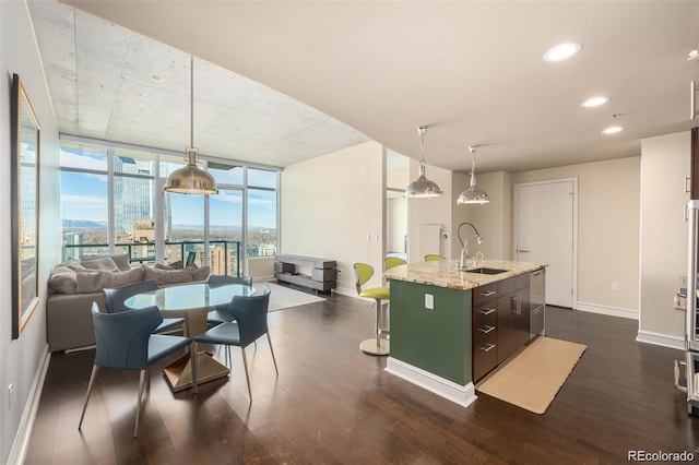 kitchen featuring sink, decorative light fixtures, expansive windows, an island with sink, and light stone countertops