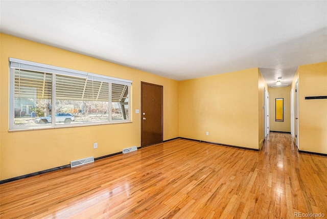 unfurnished room with light wood finished floors, visible vents, and baseboards