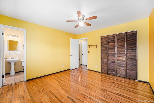 unfurnished bedroom with baseboards, ensuite bath, light wood-style flooring, ceiling fan, and a closet