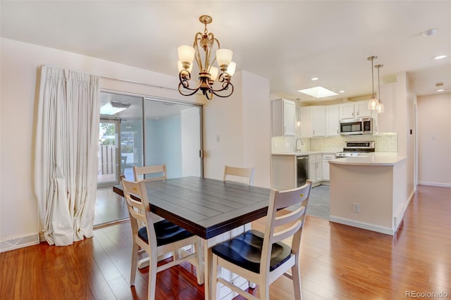 dining space with sink, light hardwood / wood-style flooring, an inviting chandelier, and a skylight