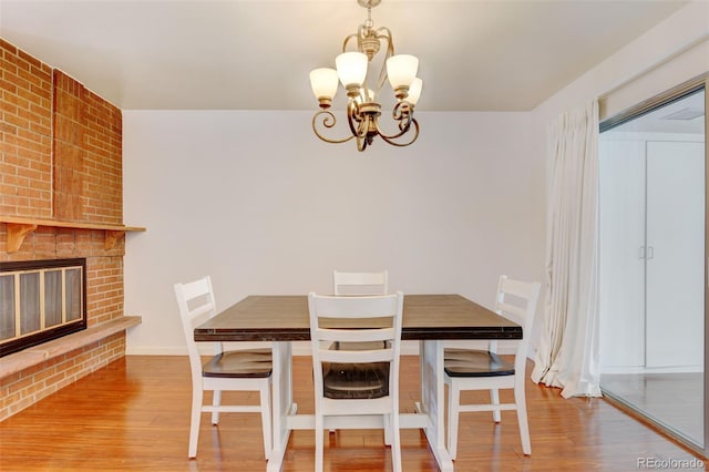 dining area featuring a notable chandelier, hardwood / wood-style flooring, and a brick fireplace