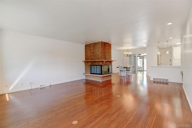 unfurnished living room with hardwood / wood-style floors, a brick fireplace, and an inviting chandelier