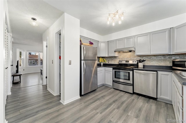 kitchen featuring gray cabinetry, decorative backsplash, a textured ceiling, light hardwood / wood-style floors, and stainless steel appliances