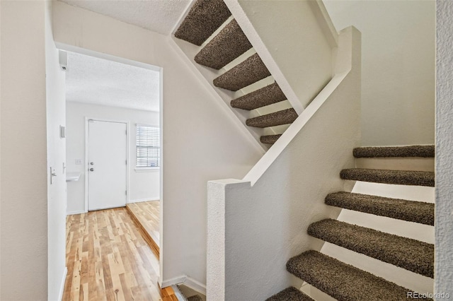 stairway with wood-type flooring and a textured ceiling