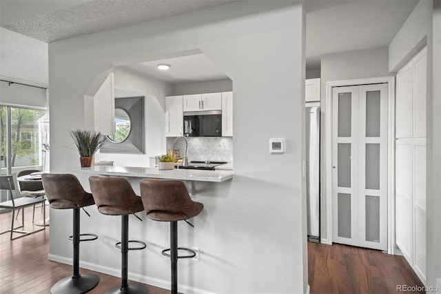 4882 W 68th Ave Unit 4, Westminster, CO 80030 - kitchen with appliances with stainless steel finishes, white cabinets, a kitchen breakfast bar, backsplash, and dark wood-style floors