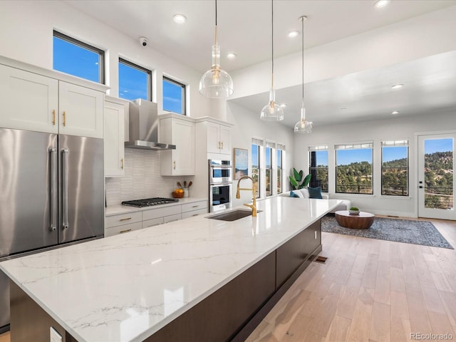 kitchen with sink, appliances with stainless steel finishes, white cabinetry, hanging light fixtures, and wall chimney exhaust hood