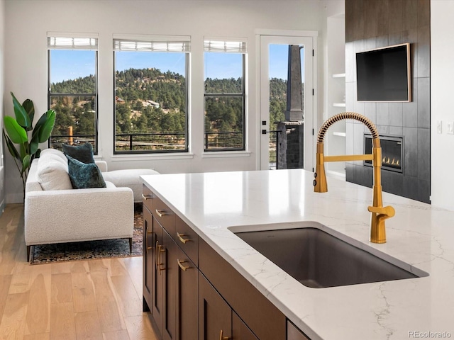 kitchen with sink, light hardwood / wood-style flooring, a tile fireplace, dark brown cabinets, and light stone countertops