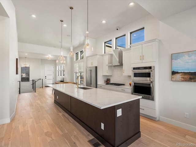 kitchen with wall chimney range hood, a large island with sink, white cabinets, and appliances with stainless steel finishes