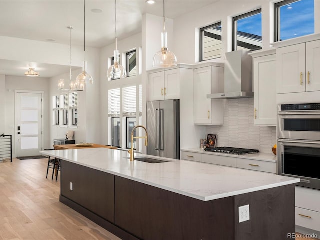 kitchen with pendant lighting, white cabinetry, sink, stainless steel appliances, and wall chimney range hood