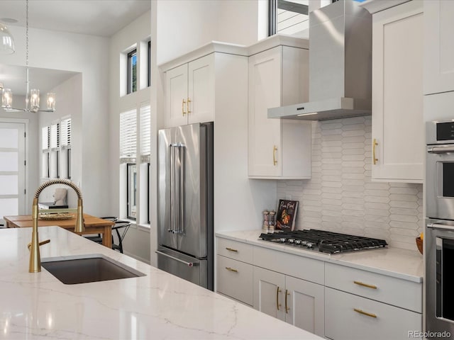 kitchen with light stone countertops, appliances with stainless steel finishes, white cabinets, and wall chimney exhaust hood