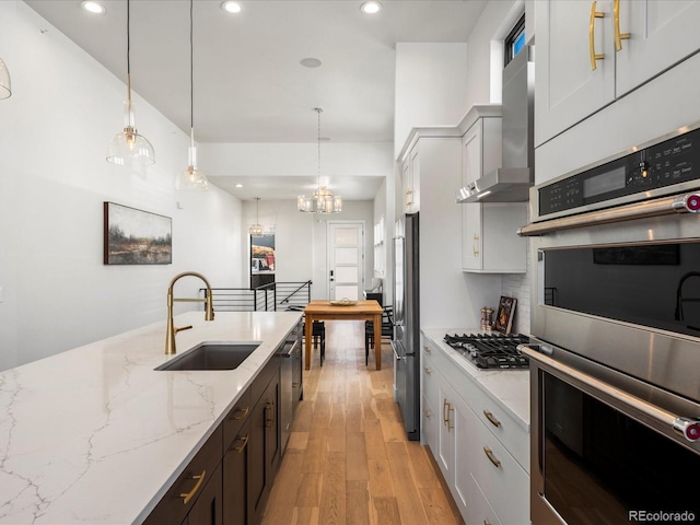 kitchen with wall chimney exhaust hood, white cabinetry, stainless steel appliances, and sink