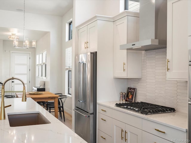 kitchen with sink, stainless steel appliances, wall chimney exhaust hood, and light stone countertops