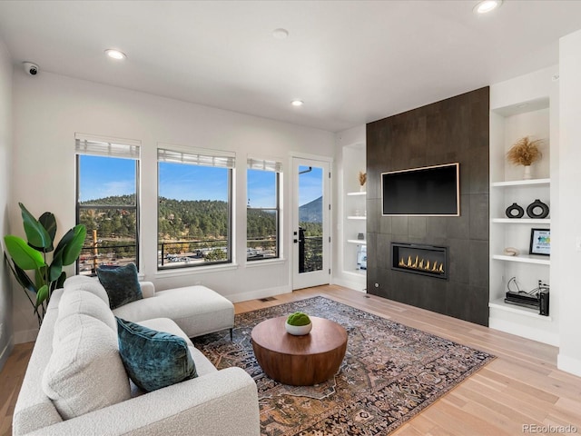 living room featuring a tile fireplace, built in shelves, and light hardwood / wood-style flooring