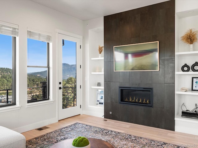 living room with a tiled fireplace, a mountain view, built in features, and light wood-type flooring