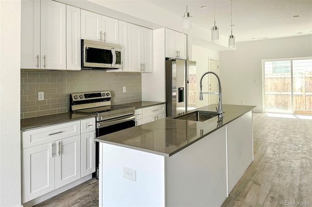 kitchen featuring backsplash, a center island with sink, appliances with stainless steel finishes, and white cabinetry