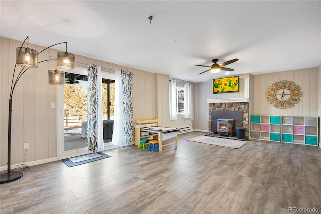 exercise room with a wood stove, ceiling fan, a baseboard heating unit, and wood walls