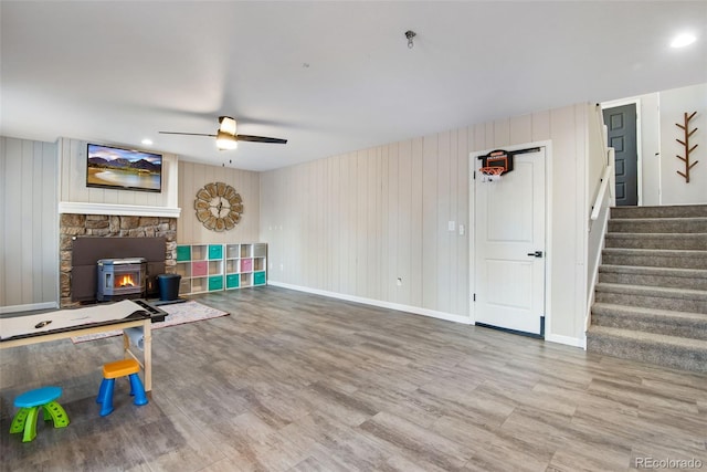 living room featuring hardwood / wood-style flooring, ceiling fan, wood walls, and a wood stove