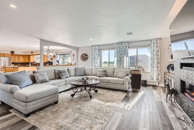 living area featuring a chandelier, a textured ceiling, wood finished floors, visible vents, and a tiled fireplace