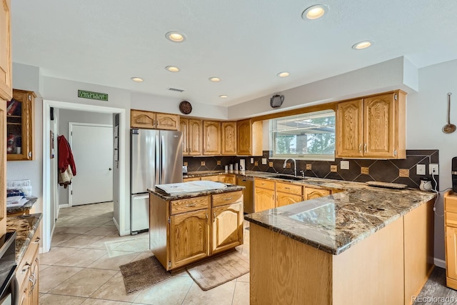 kitchen featuring tasteful backsplash, dark stone countertops, a center island, stainless steel appliances, and a sink