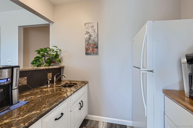 kitchen featuring baseboards, white cabinets, dark stone counters, freestanding refrigerator, and a sink