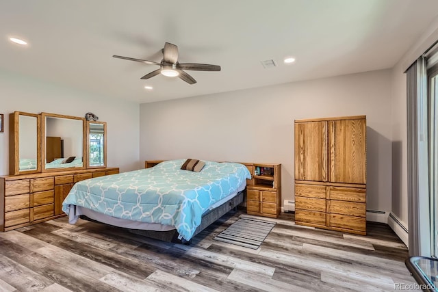 bedroom with a baseboard heating unit, wood finished floors, visible vents, and recessed lighting