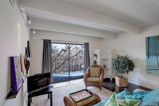 living room featuring beam ceiling, wood finished floors, baseboards, and a textured ceiling