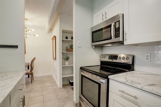 kitchen featuring light tile patterned floors, light stone countertops, stainless steel appliances, decorative backsplash, and white cabinetry