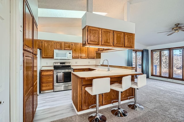 kitchen featuring white microwave, a breakfast bar area, stainless steel range with electric cooktop, a peninsula, and a sink