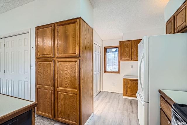 kitchen featuring brown cabinets, light wood-style flooring, a textured ceiling, freestanding refrigerator, and stainless steel electric range