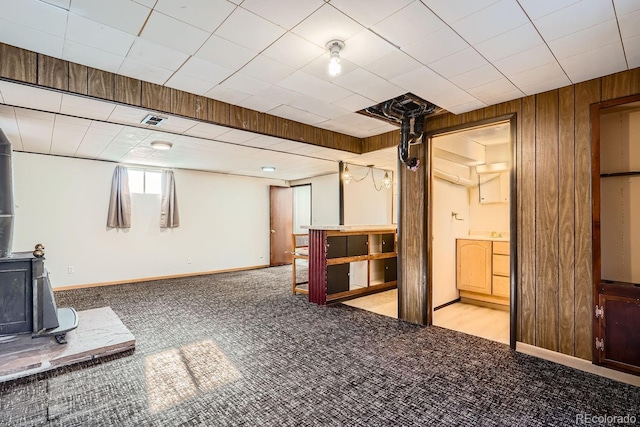 below grade area featuring wooden walls, visible vents, baseboards, carpet floors, and a wood stove